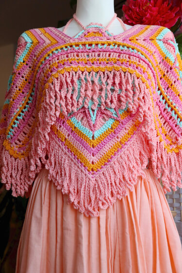 Gehäkelter Poncho in Rosa, Orange und Hellblau mit Fransen und V‑Muster auf einer Schaufensterpuppe