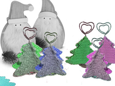 Gehäkelte, bunte Tannenbaum-Memohalter mit herzförmigen Clips vor zwei Weihnachtsmann-Figuren in Grautönen.