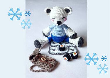 Gehäkelter weißer Eisbär in blauem Outfit mit drei Mini-Sushi und brauner gehäkelter Tasche auf einer Matte