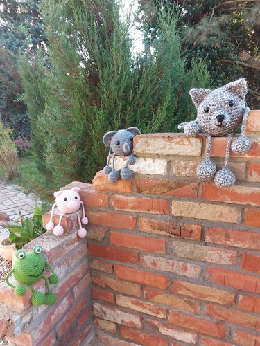 Vier gehäkelte Amigurumi (Koala, Frosch, Schwein, Kätzchen) auf einer Ziegelmauer