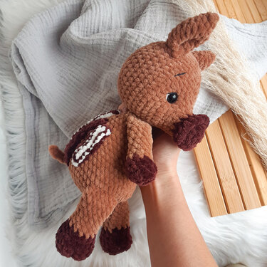 Braunes gehäkeltes Amigurumi-Rehkitz mit weißen Punkten und dunklen Hufen, in Hand gehalten