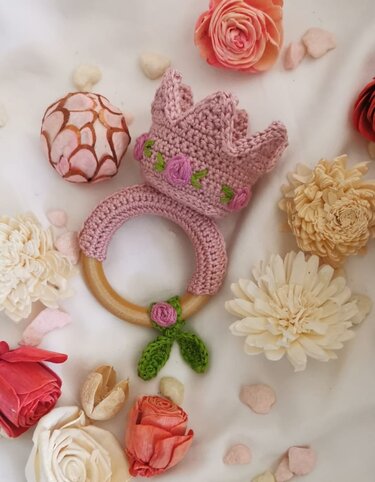 Gehäkelte rosa Krone auf Holzgreifring mit Rosen-Applikationen, umgeben von Blumen
