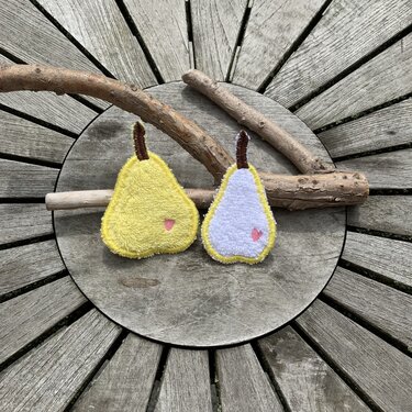 Zwei Birnen-Anhänger aus Stoff, gelb und weiß, mit rosa Herz und braunem Stiel auf einer runden Holzplatte