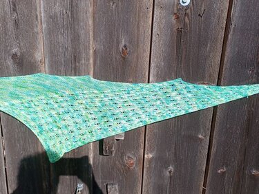 Gestricktes Dreieckstuch in Grün und Türkis mit Lochmuster vor einer Holzwand