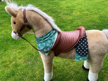 Nahaufnahme: brauner Sattelüberzug mit grüner Halstuchkante und schwarzer, gepunkteter Satteltasche an Plüschpony