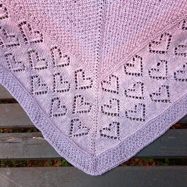 Gestricktes Dreieckstuch mit Herz-Lochmuster in Rosa- und Lilatnen auf einer Holzbank