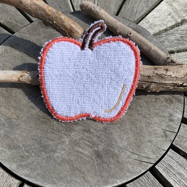 Weiße Apfel-Applikation aus Frottee mit orangem Rand und braunem Stiel auf Holzuntergrund