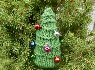 Kleiner grüner gestrickter Tannenbaum mit bunten Glöckchen vor Nadelbaumzweigen