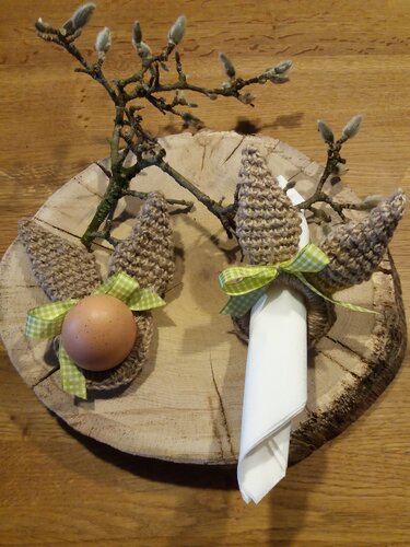 Handgehäkelte Hasenohren als Eierwärmer und Serviettenring mit grün-kariertem Band auf Holzscheibe mit Weidenkätzchen