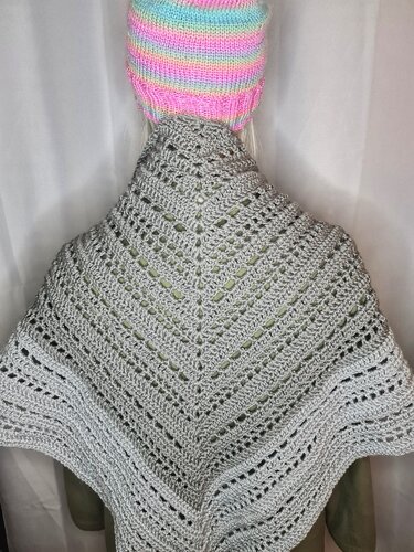 Rückansicht eines grauen gehäkelten Dreiecksschals mit Reihen aus Lochmuster und einer bunten Mütze