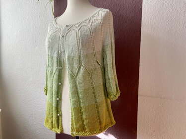 Gestrickter Damen-Cardigan in Creme- und Grüntönen mit Lochmuster und Knopfleiste auf einer Schneiderpuppe