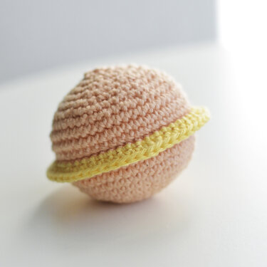 Nahaufnahme eines selbstgehäkelten Saturn-Balls in Beige mit gelbem Ring.