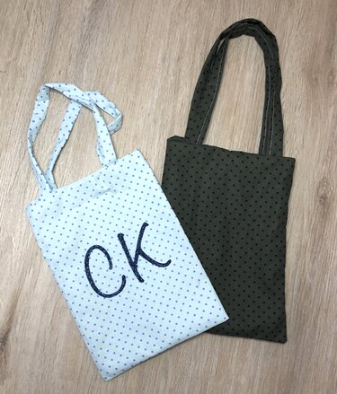 Zwei Utensilo-Taschen aus gepunktetem Stoff, hellblau mit gestickter Verzierung und dunkelgrün mit schwarzen Punkten.
