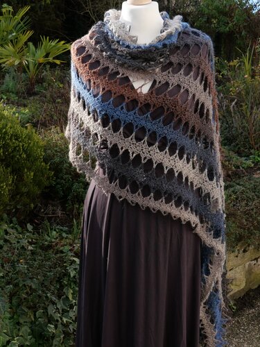 Gehäkeltes Tuch mit großem Lochmuster in Grau, Blau und Braun, auf einer Schaufensterpuppe drapiert.