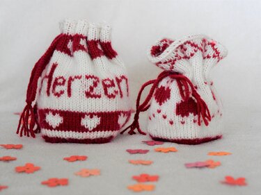 Zwei handgestrickte Zugbeutel rot-weiß mit Herzmotiven und Schriftzug Herzen auf hellem Hintergrund