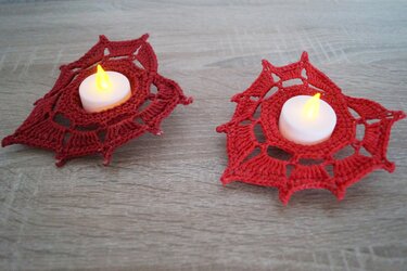 Zwei rote gehäkelte Stern-Untersetzer mit LED-Teelichtern auf heller Holzoberfläche
