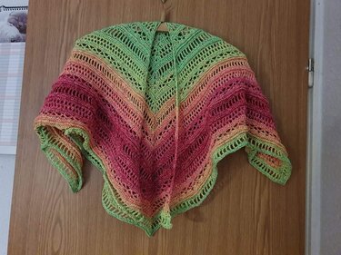 Gehäkeltes Dreieckstuch in Grün, Orange und Pink, an einer Holztür aufgehängt.