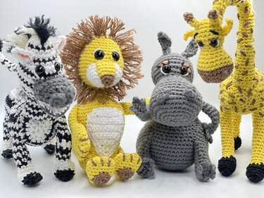 Vier gehäkelte Amigurumi-Tiere: Zebra, Löwe, Nilpferd und Giraffe vor hellem Hintergrund.