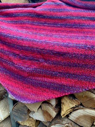 Gestricktes Dreieckstuch mit breiten Querstreifen in Pink, Lila und Rot auf Holzscheiten