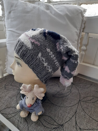 Gestrickte Kindermütze in Grau, Weiß, Rosa und Dunkelblau mit langem Zipfel und rosa Bommel auf einer Schaufensterpuppe.