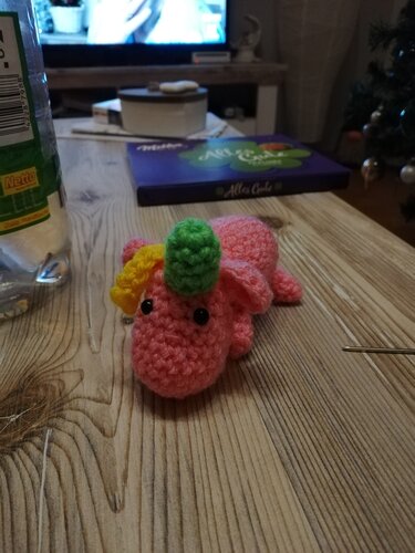 Pinkes gehäkeltes Einhorn-Amigurumi mit grünem Horn und gelber Mähne auf Holztisch