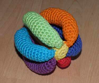 Handgehäkelter Greifball in Regenbogenfarben auf Holzoberfläche