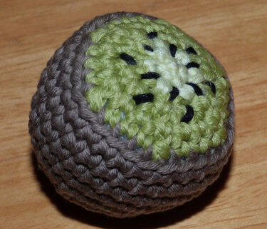 Nahaufnahme einer handgehäkelten Kiwi mit brauner Schale und grünem Fruchtfleisch