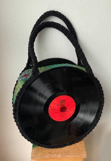 Runde Handtasche mit schwarzen Schallplatten als Seiten, grün gehäkeltem Korpus und schwarzen Griffen.