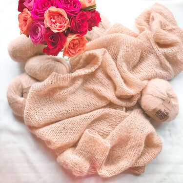 Leichtes Strickteil in Rosé mit Garnknäueln und Rosen auf hellem Hintergrund