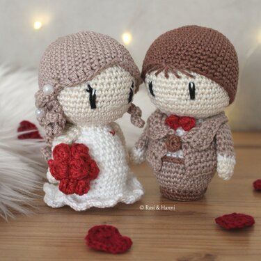 Gehäkeltes Amigurumi-Brautpaar mit rotem Strauß und braunem Anzug auf Holzuntergrund