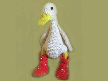 Close-up of crocheted duck showing body texture, yellow beak and red crochet boots