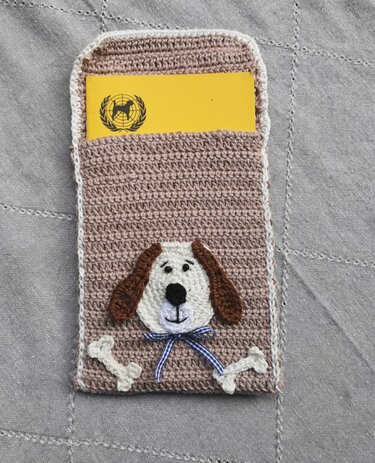 Taupefarbene, schmale gehäkelte Kartenhülle mit appliziertem Hundegesicht und Knochenapplikationen