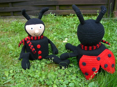 Zwei gehäkelte Käfer-Amigurumi, ein roter Marienkäfer und ein schwarzer Käfer, im Gras