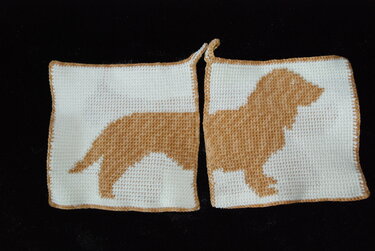 Two square white crochet potholders forming a tan dog silhouette with tan edging and hanging loops