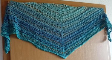 Gehäkeltes Dreieckstuch in Blau- bis Grüntönen mit Lochmuster, an einer Tür hängend