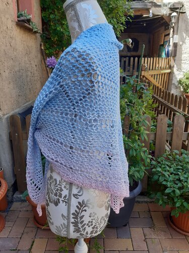 Fein gehäkeltes Tuch mit Farbverlauf von Hellblau zu Rosa und luftigem Lochmuster auf einer Schneiderpuppe im Garten