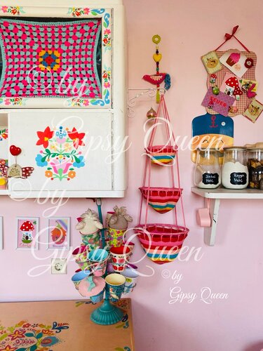 Farbenfrohe Häkeldecke, hängende Utensilo-Körbe und ein Tassenständer vor einer rosa Wand