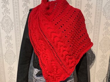 Rotes gestricktes Dreieckstuch mit Zopf- und Lochmuster, über einer dunklen Jacke drapiert.