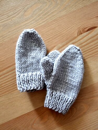 Zwei graue gestrickte Baby-Fäustlinge auf Holzuntergrund