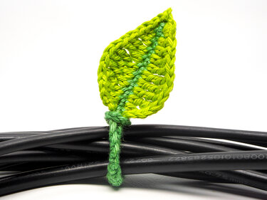 Bright green crocheted leaf cable tie bundling black cables on a white background.