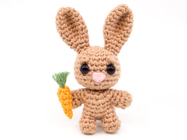 tan crocheted amigurumi bunny with carrot on white background