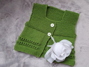 Grüne gestrickte Babyweste mit zwei weißen Knöpfen auf hellgrauem Stoff