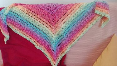 Gehäkeltes Dreieckstuch in Pastell-Regenbogen mit Reihen aus Lochmuster, über eine Sofalehne gelegt