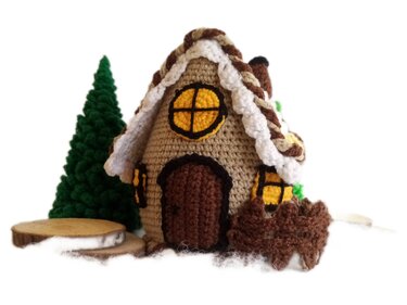 Crocheted gingerbread house with green Christmas tree and wooden slices on a white background.