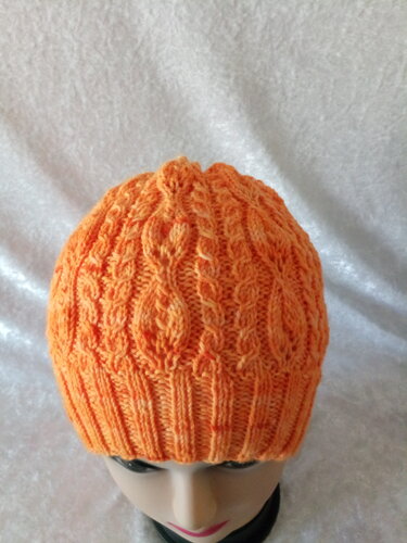 Orangefarbene Strickmütze mit Zopfmuster auf Schaufensterpuppe