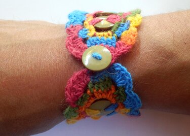 Mehrfarbiges gehäkeltes Armband mit drei hellen Knöpfen am Handgelenk