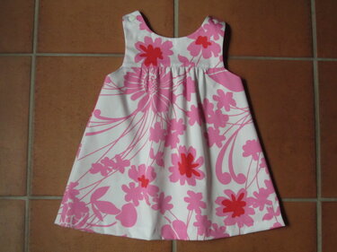 A-Linien-Kinderkleid mit rosa-pink Blumenprint und Schulterknöpfen, auf Fliesenboden liegend
