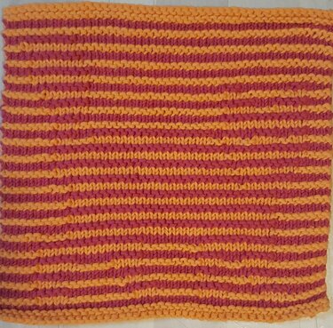 Quadratisches gestricktes Stück im Krausrippenmuster mit feinen horizontalen Streifen in Orange und Rosa.