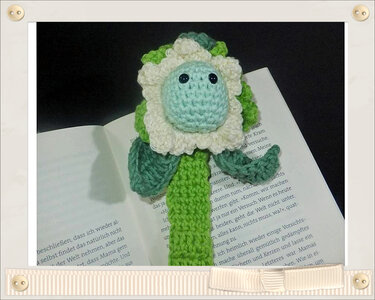 Gehäkeltes Blumen-Lesezeichen in Grün, Weiß und Hellblau in einem geöffneten Buch
