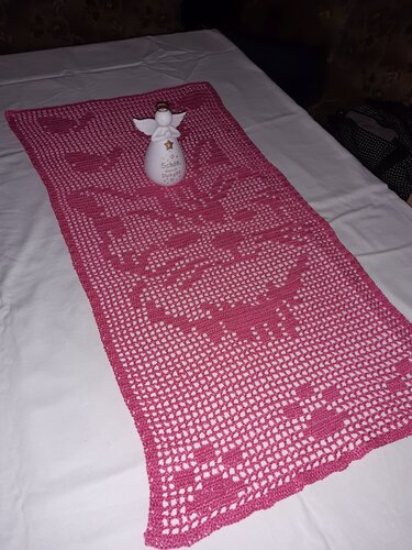 Rosa gehäkelter Filet‑Tischläufer mit Herzmuster auf weißer Unterlage, dekoriert mit kleiner Engel‑Figur